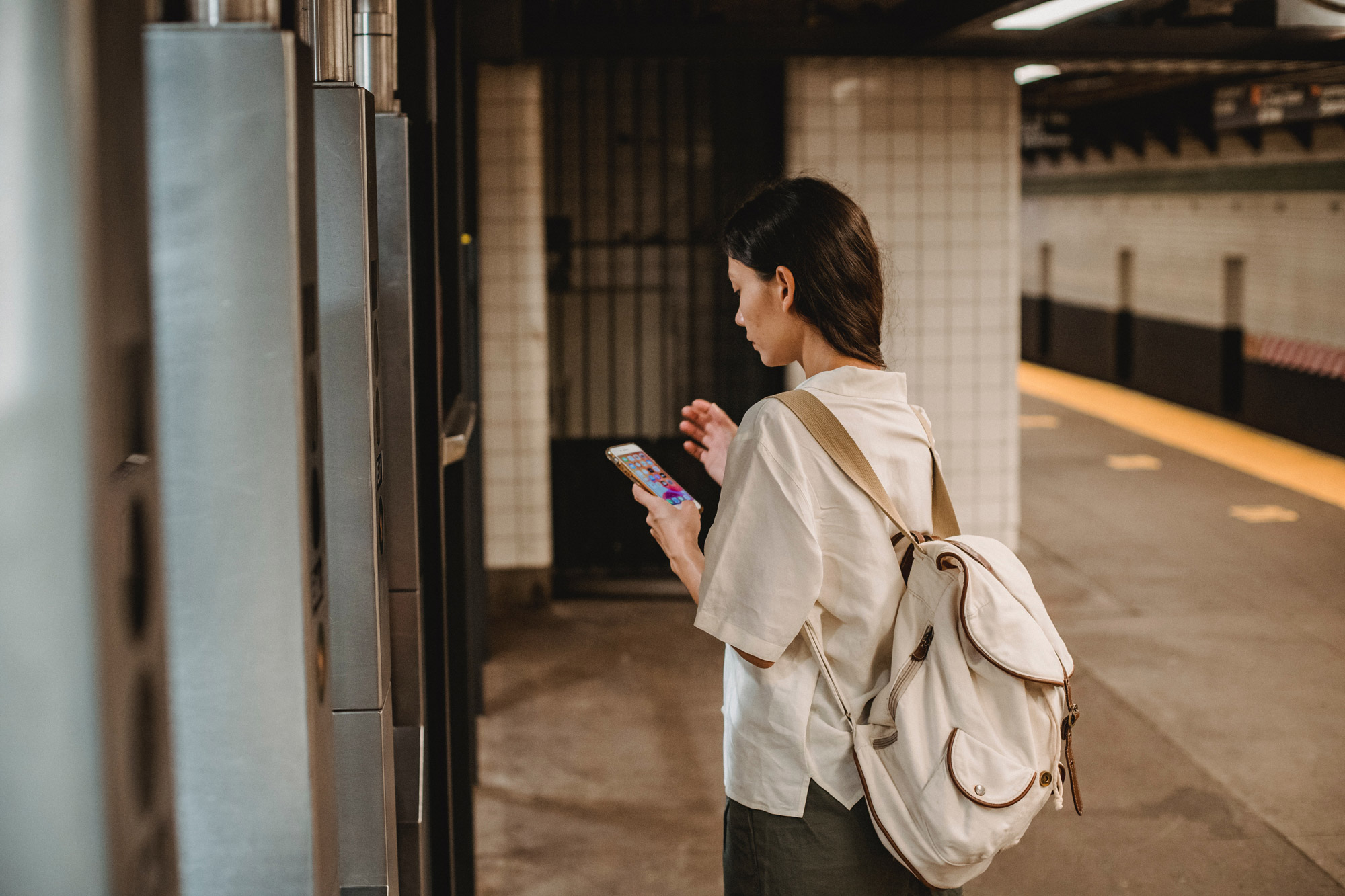 A woman pauses to look at her phone before going through the subway turnstiles to leave the subway