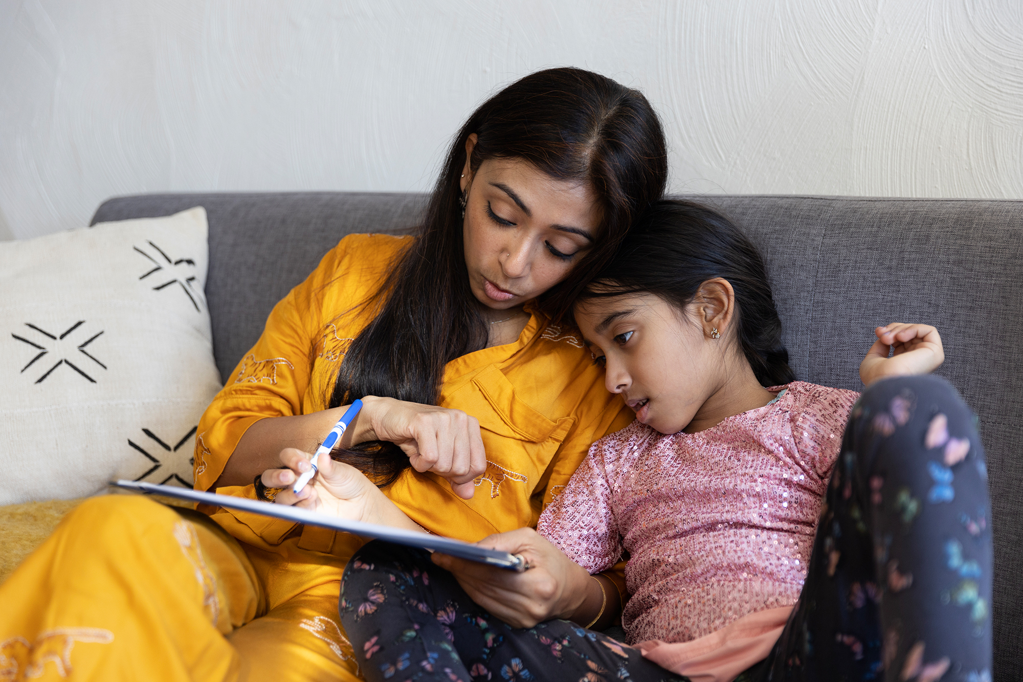 A mother and daughter color together on the couch