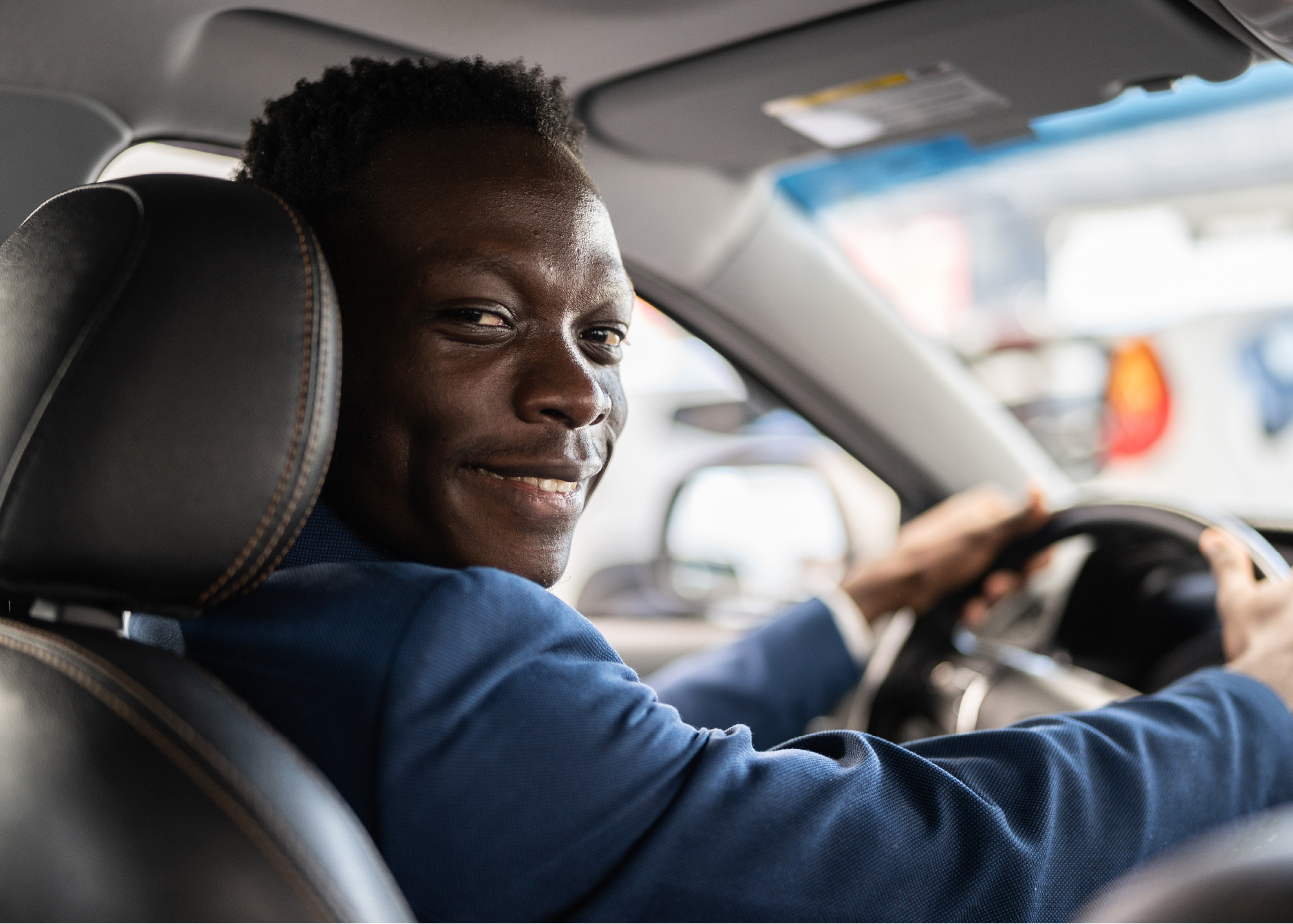 A man driving a car, turns towards the back seat and smiles.